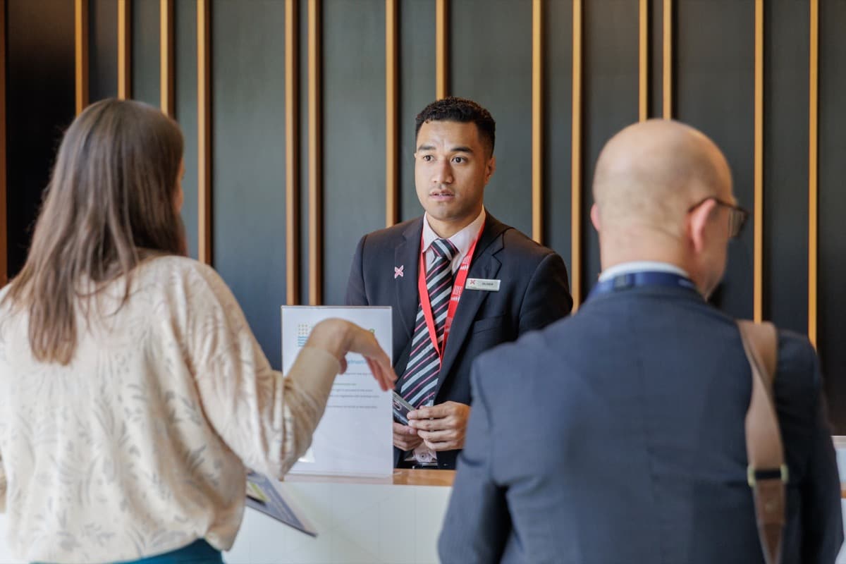 A concierge staff member answers questions from two delegates at an information desk