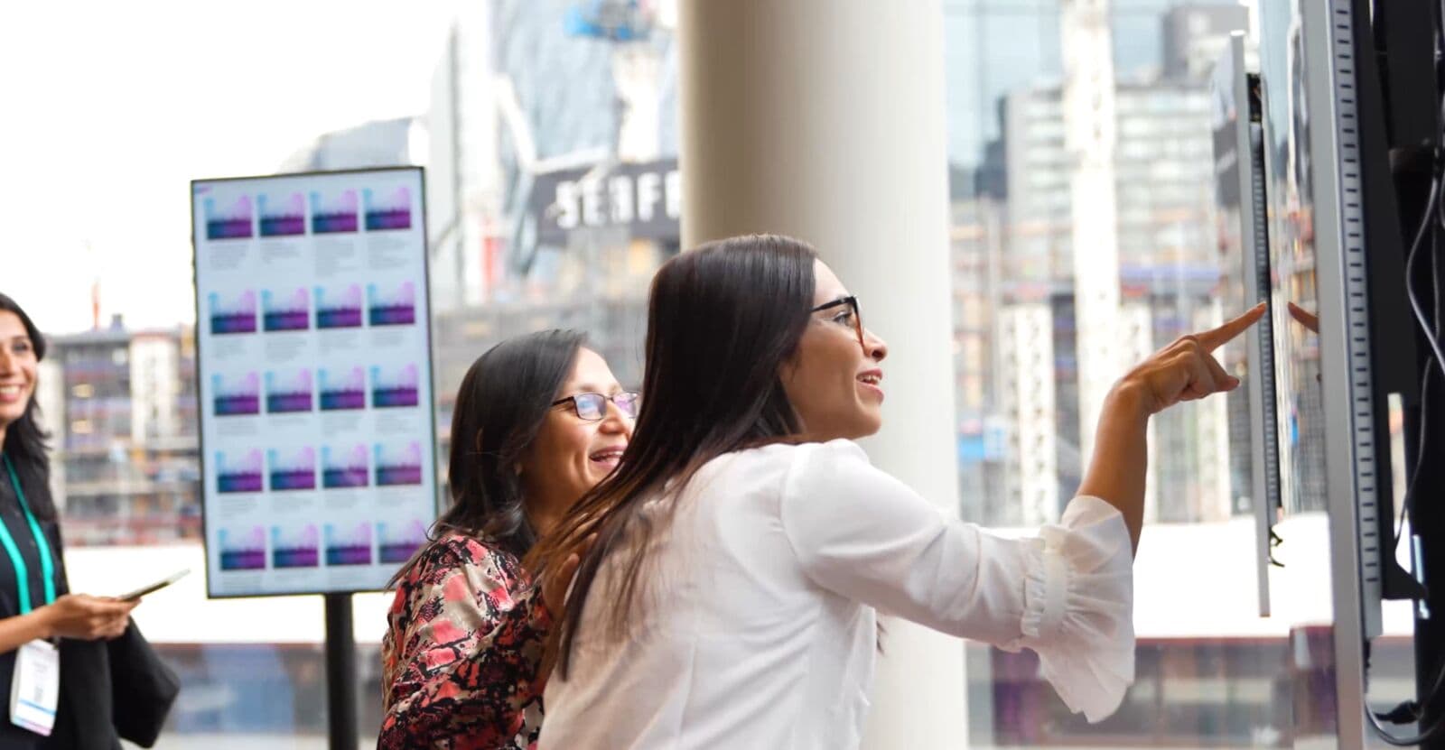 Two delegates point at an interactive e-poster touchscreen in a conference foyer